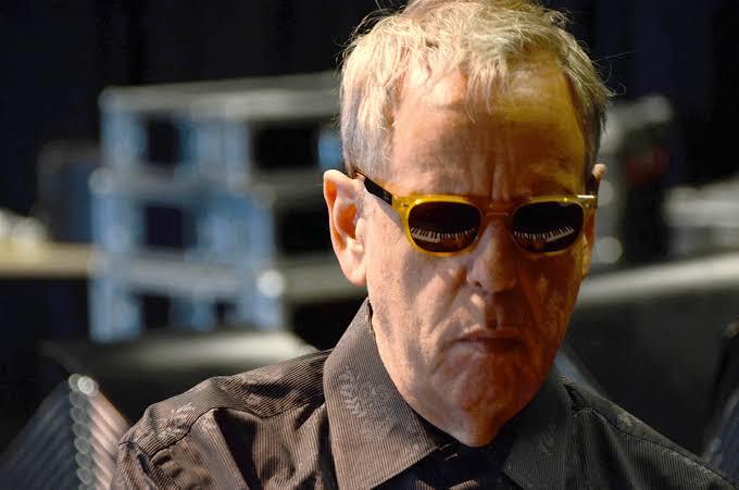 Photo of man with glasses. Piano keys are reflected in his glasses.