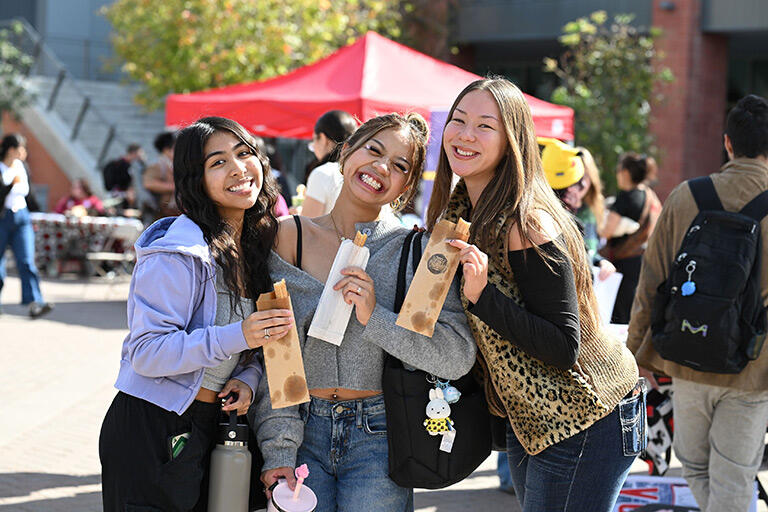 Three students smile while holding snacks