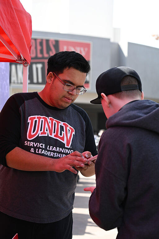 A student wearing a UNLV shirt assists a person