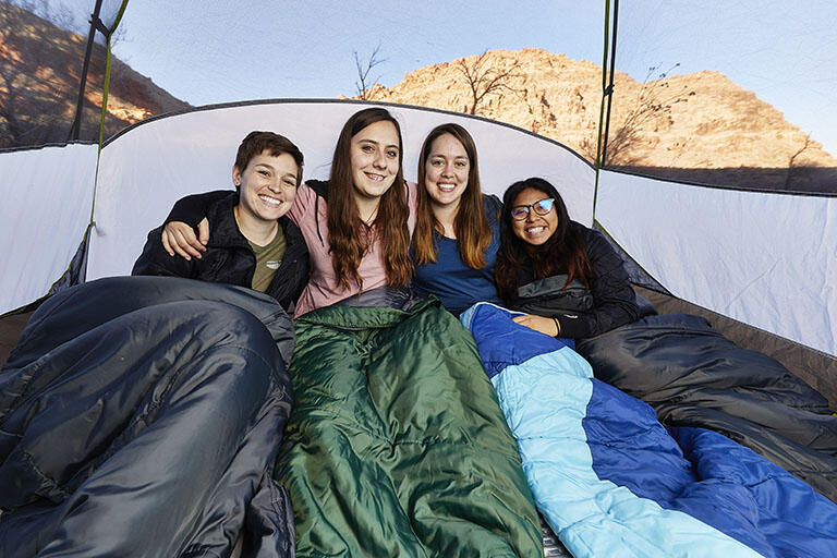 Four students in a tent and sitting in sleeping bags.