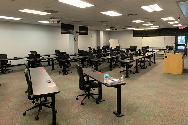 An classroom with rows of tables and chairs facing a podium.