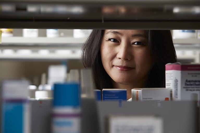 A pharmacist in a pharmacy surrounded by various bottled medication.