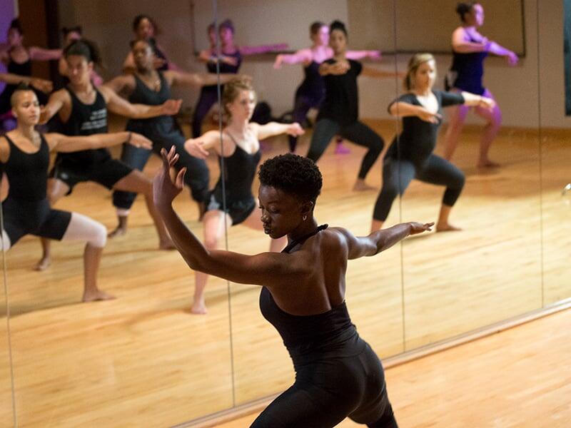 Woman in a graceful dance pose in front of a mirror showing a reflection of a class full of women in a dance poses