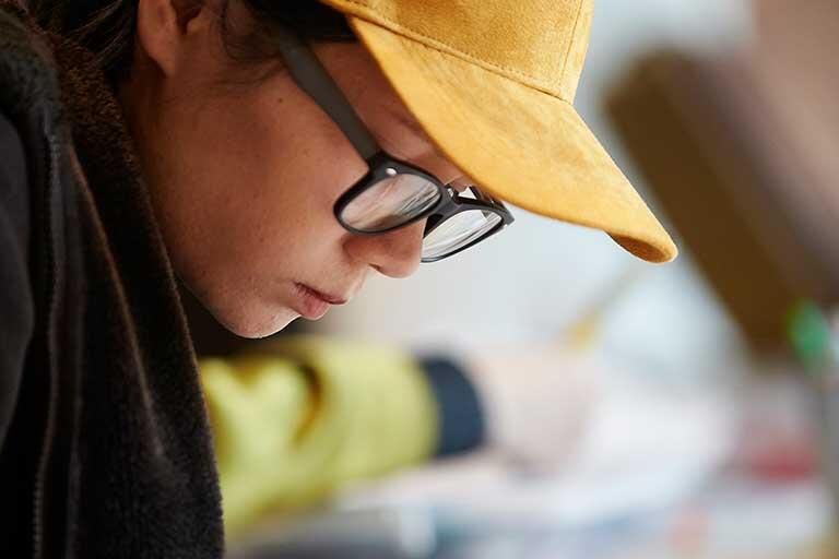 Student with yellow cap focuses intently on their drawing