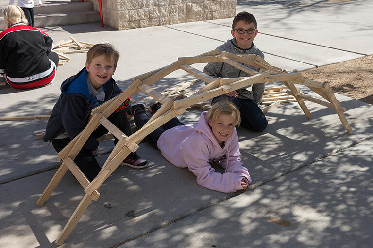 Three children surrounding a wooden bridge.