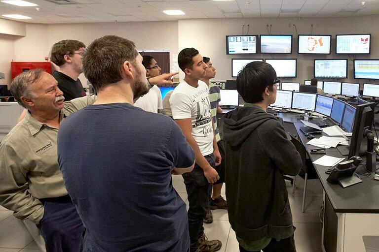 Men gather around computer screens.