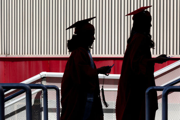Two students walk with diploma in hand