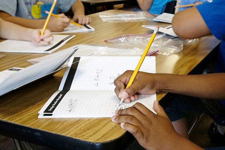 View of hands writing in a lesson book.
