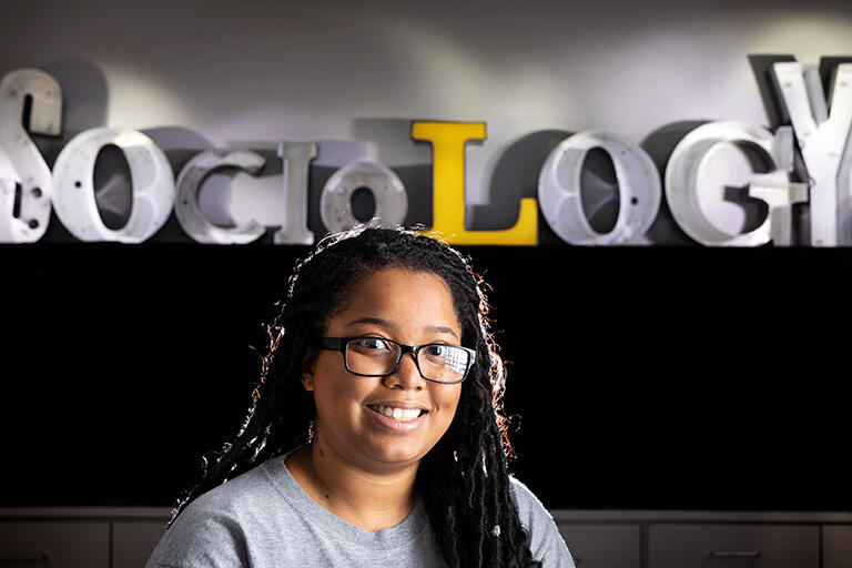 A woman standing in front of a sign that spells out "Sociology"