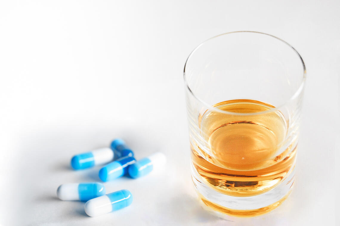 Pills next to a cup filled with alcohol