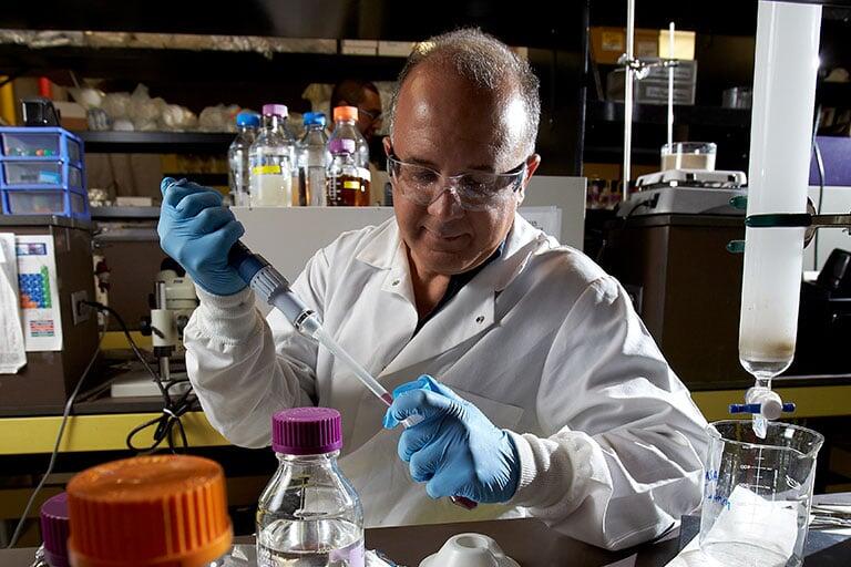 Faculty member puts liquid into a test tube.