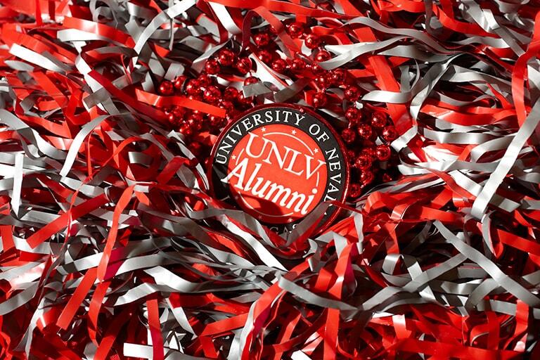 A UNLV Alumni badge surrounded by red and gray confetti