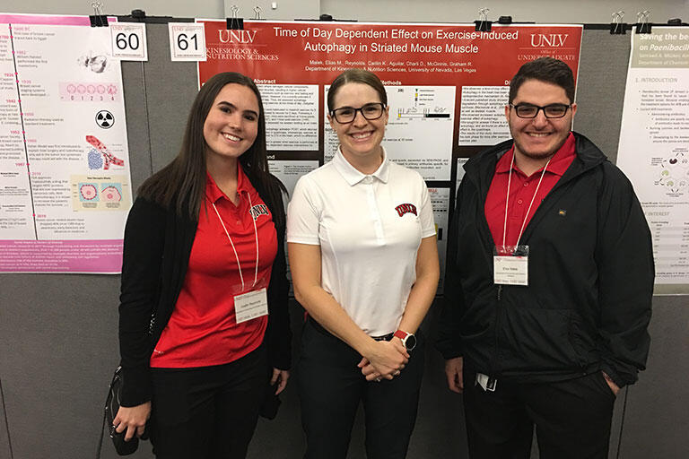 Three students smiling in front of their poster