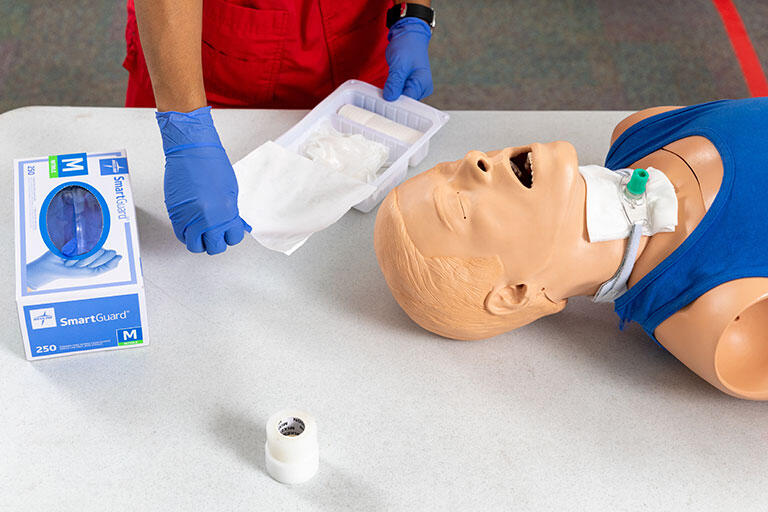 A hospital training manikin with a student working on it.