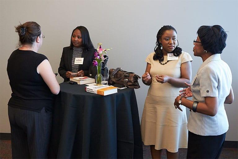Four women standing around a high table talking to each other in pairs
