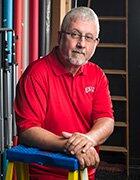 Joe Aldridge wearing a collared red UNLV shirt and leaning against a ladder