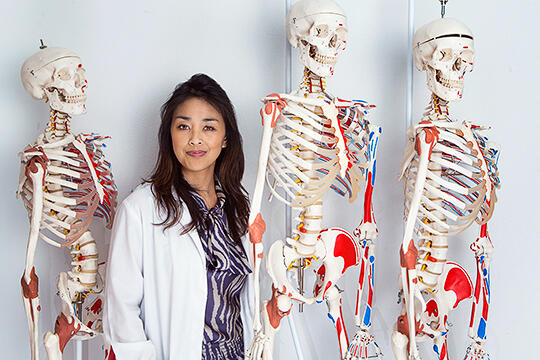 Jennifer Kawi poses next to three skeletons