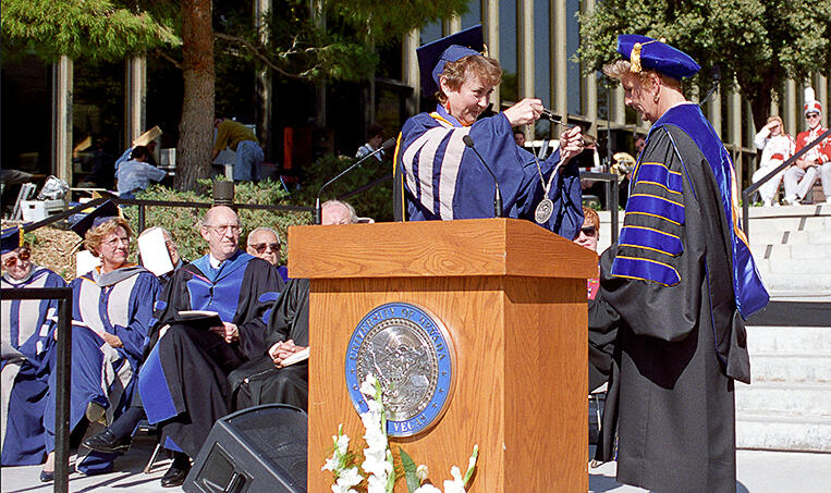 Two people standing at the podium. One is handing the other a token of inauguration as UNLV president in 1995.