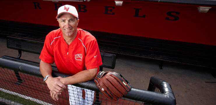 A man wearing a baseball hat and red polo shirt leaning against a pole barrier