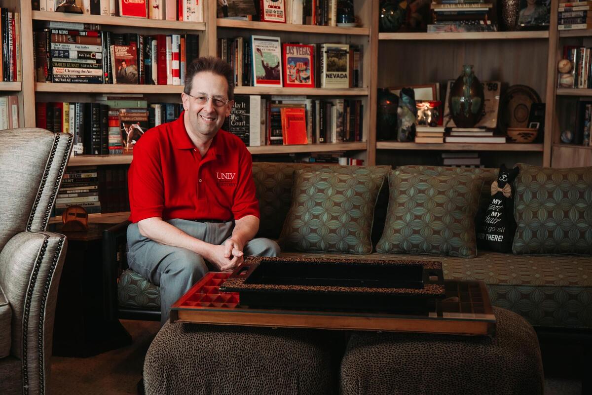 A man sits in front of wall-to-wall bookshelves