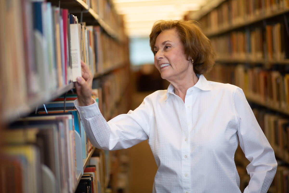 A woman looks at a book on a library shelf