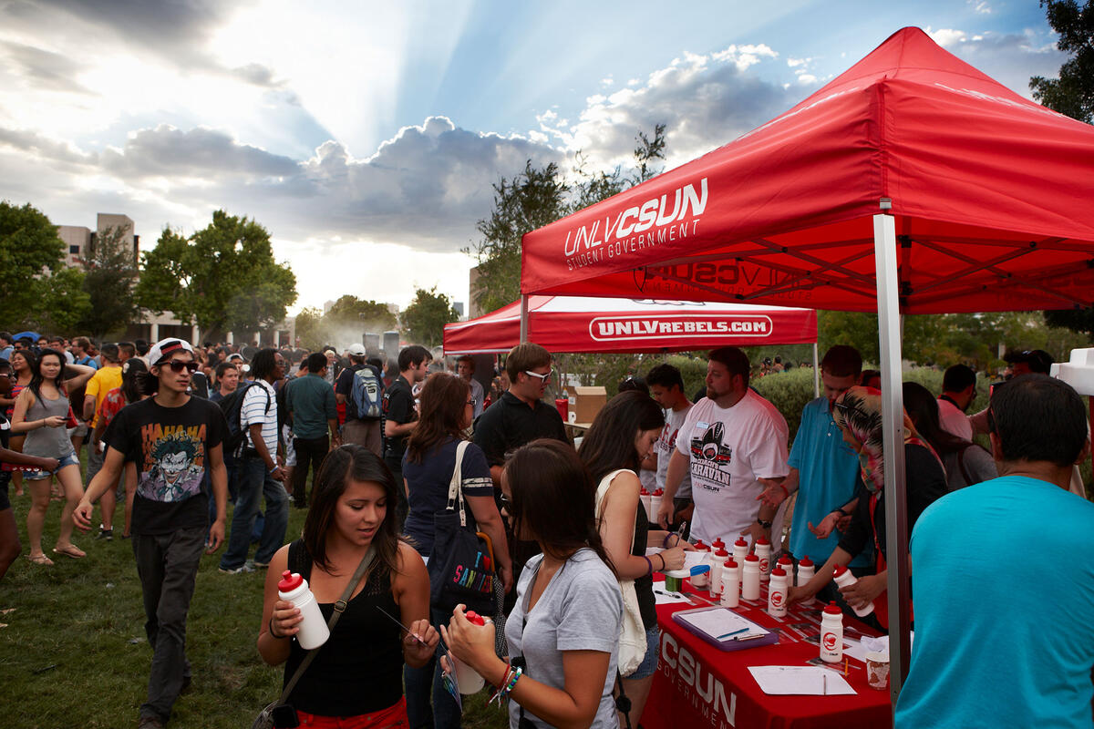 Students gathered by a tent on a beautiful cloudy after noun.