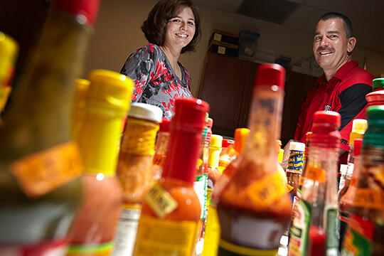 Two people looking at a variety of hot sauces on a table