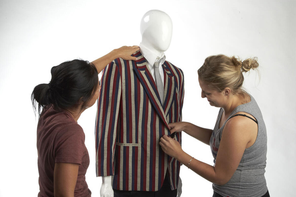 Two women measuring a coat on a mannequin