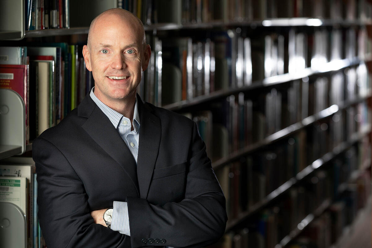 Cory Tucker standing in Lied Library in front of a book shelf.