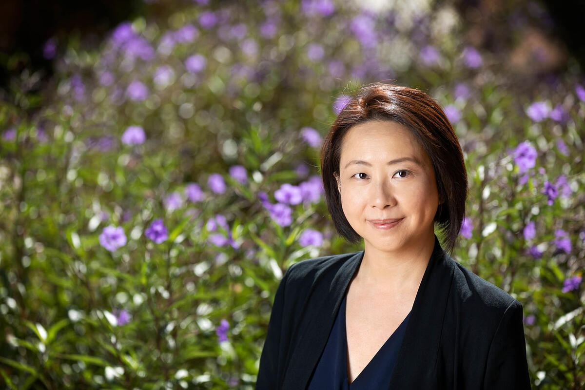 Shelly Wang the director of program development for Continuing Education poses in front of flowers.