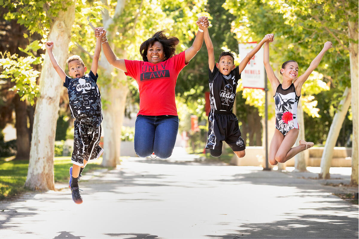 Nakia Jackson-Hale holding hands with her three kids and jumping in the air outside.