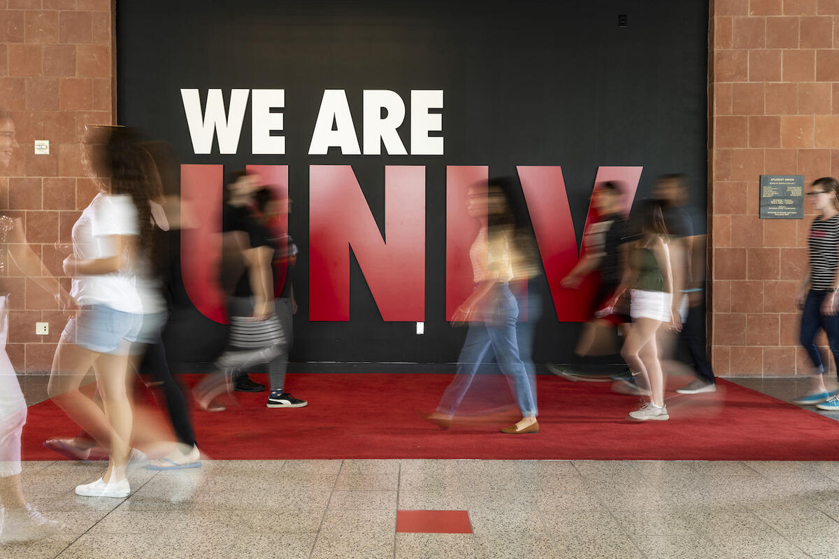 Blurred students walking by We Are U.N.L.V. poster