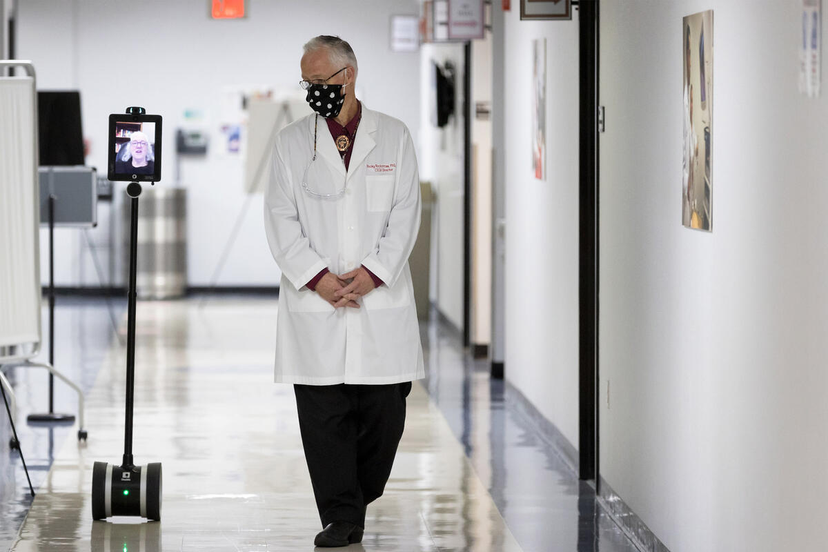 man walking through hallway next to a screen moving on robotic wheels