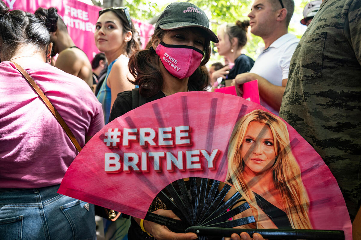 A woman holds a pink fan featuring Britney Spears' face and the words &quot;Free Britney&quot;