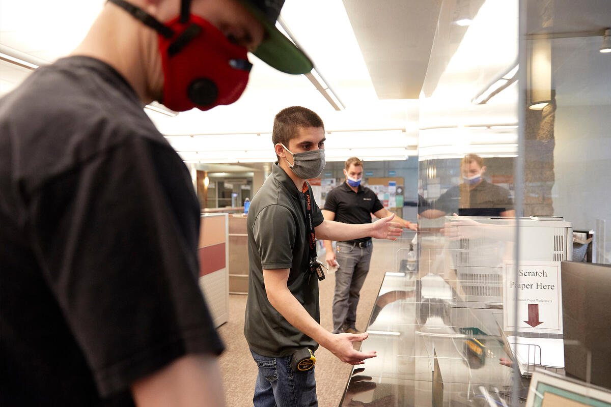 Three workers in masks install plexiglass