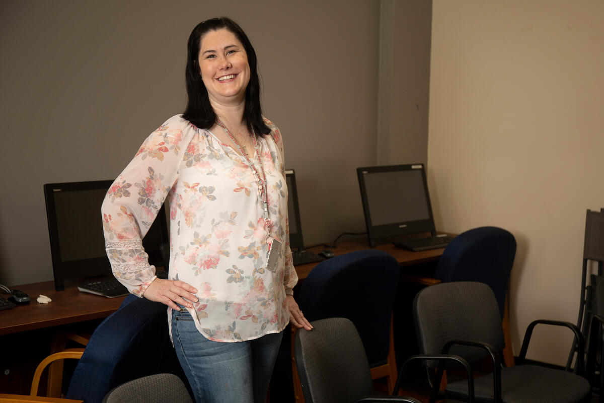 A woman in a flower print shirt stands in front of a row of computers