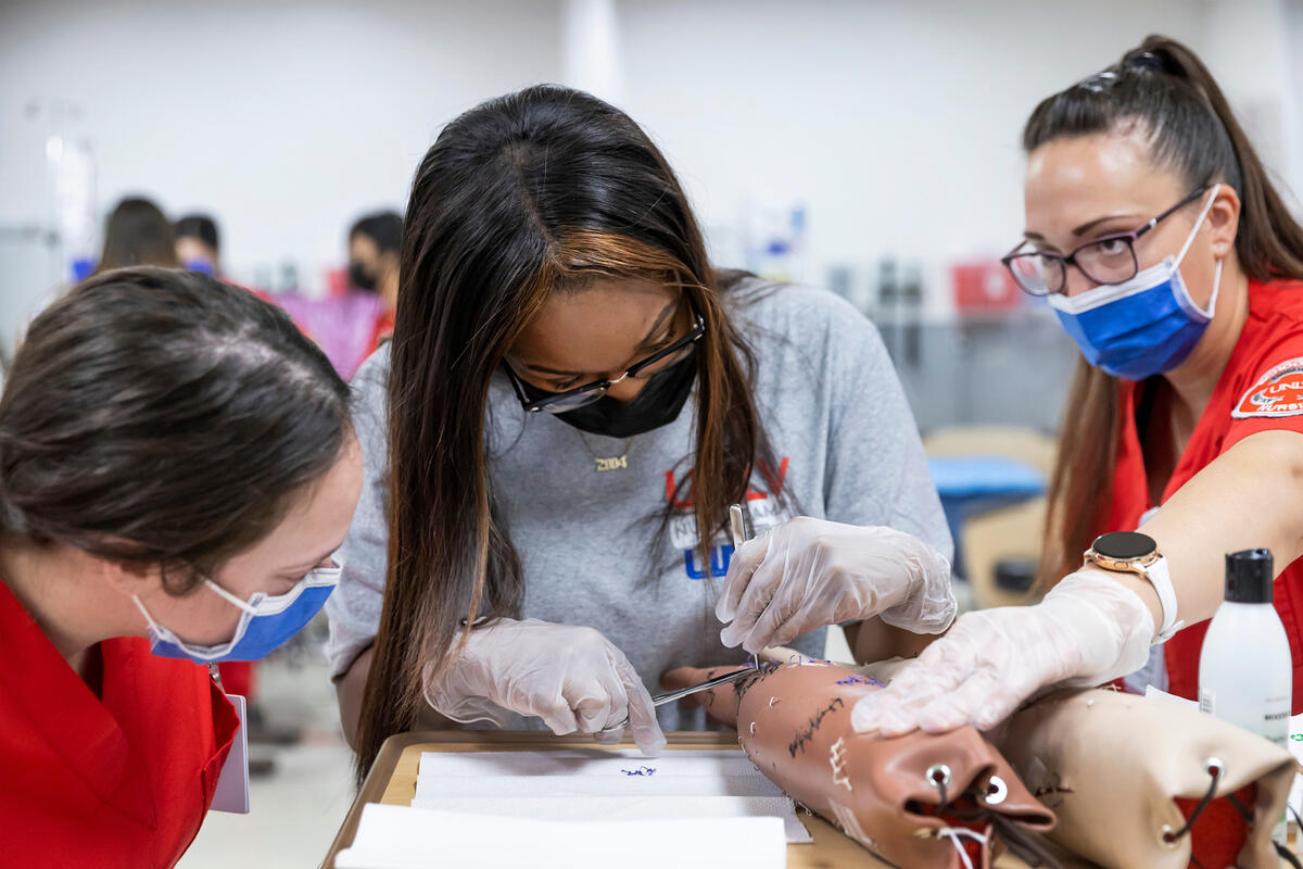 Three students work on removing sutures from a plastic arm