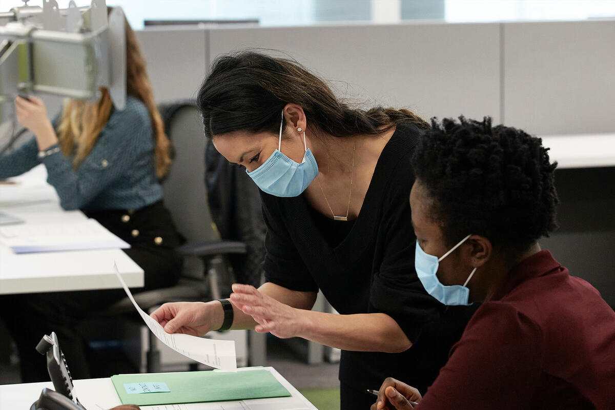 Two women wearing surgical masks look over paperwork