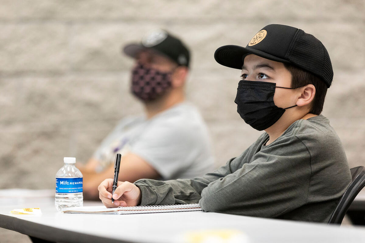 Young student wears a mask while taking notes in a classroom