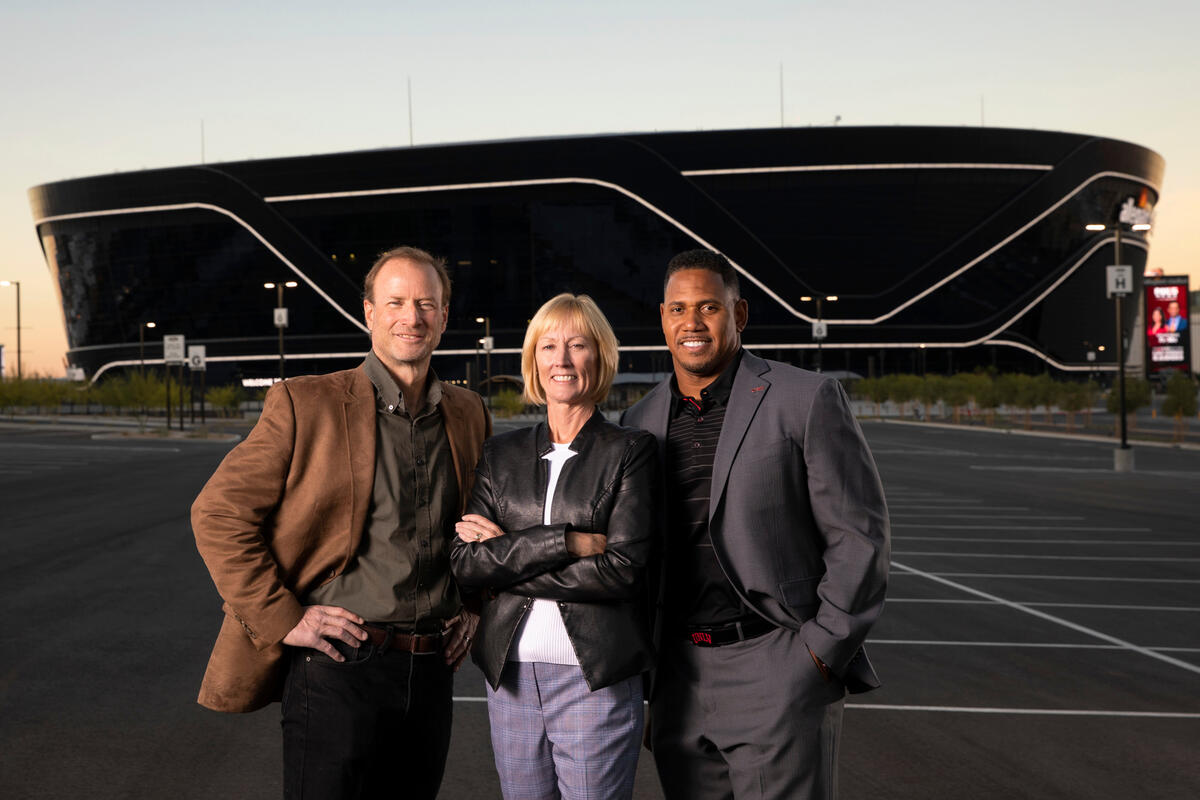 Three people stand framed by Allegiant Stadium in the background.