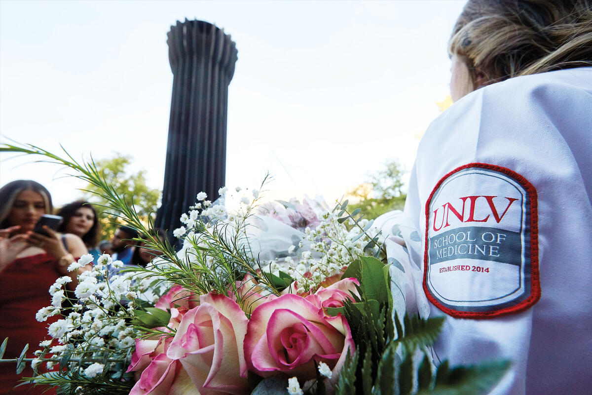 A student wears a white coat with a patch that reads 'UNLV School of Medicine'