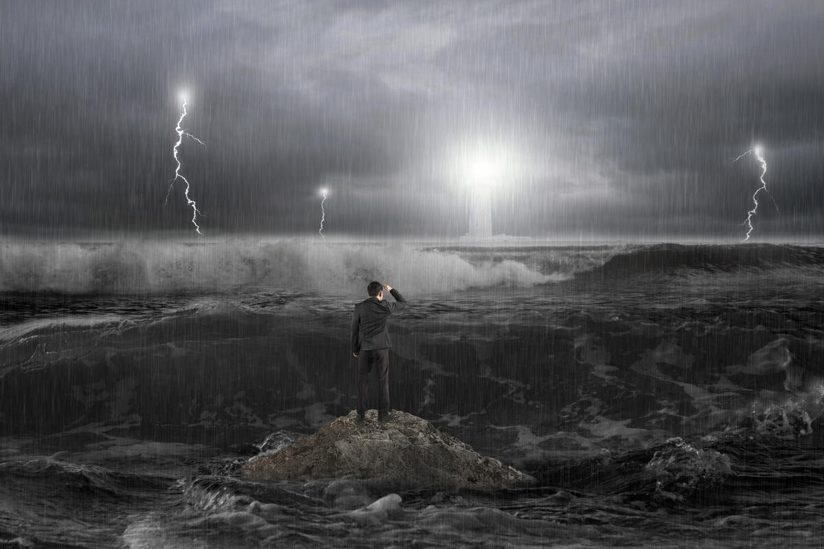 Man on rock gazing at lighthouse in the ocean with storm, thunder, lightening and waves in dark