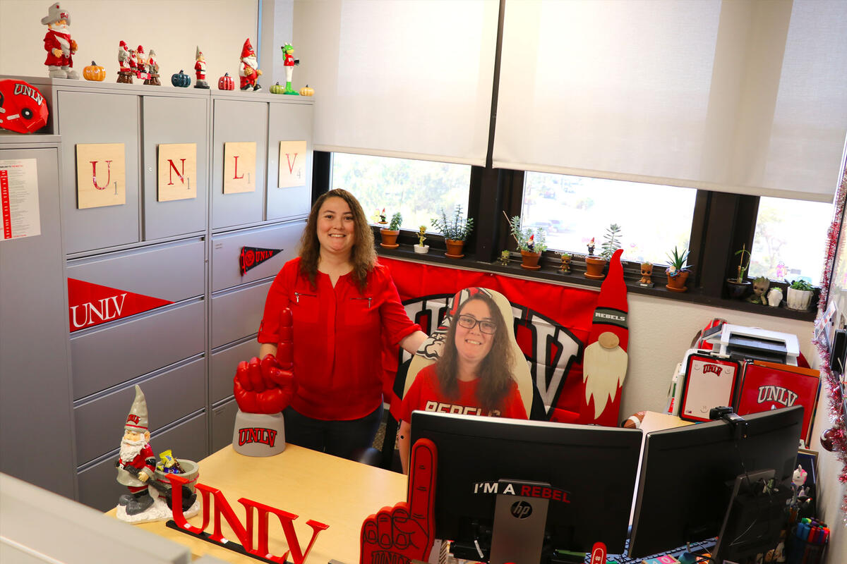A woman stands in her office surrounded by UNLV memorabilia