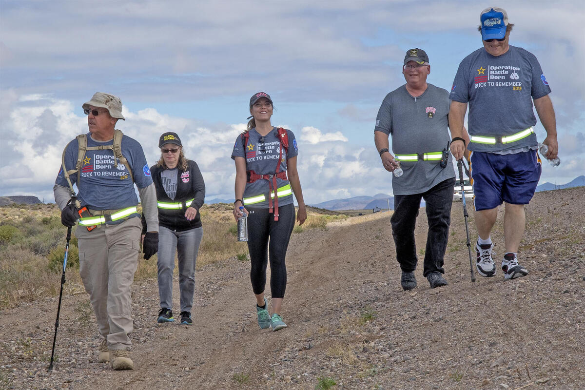 five people marching on side of desert road