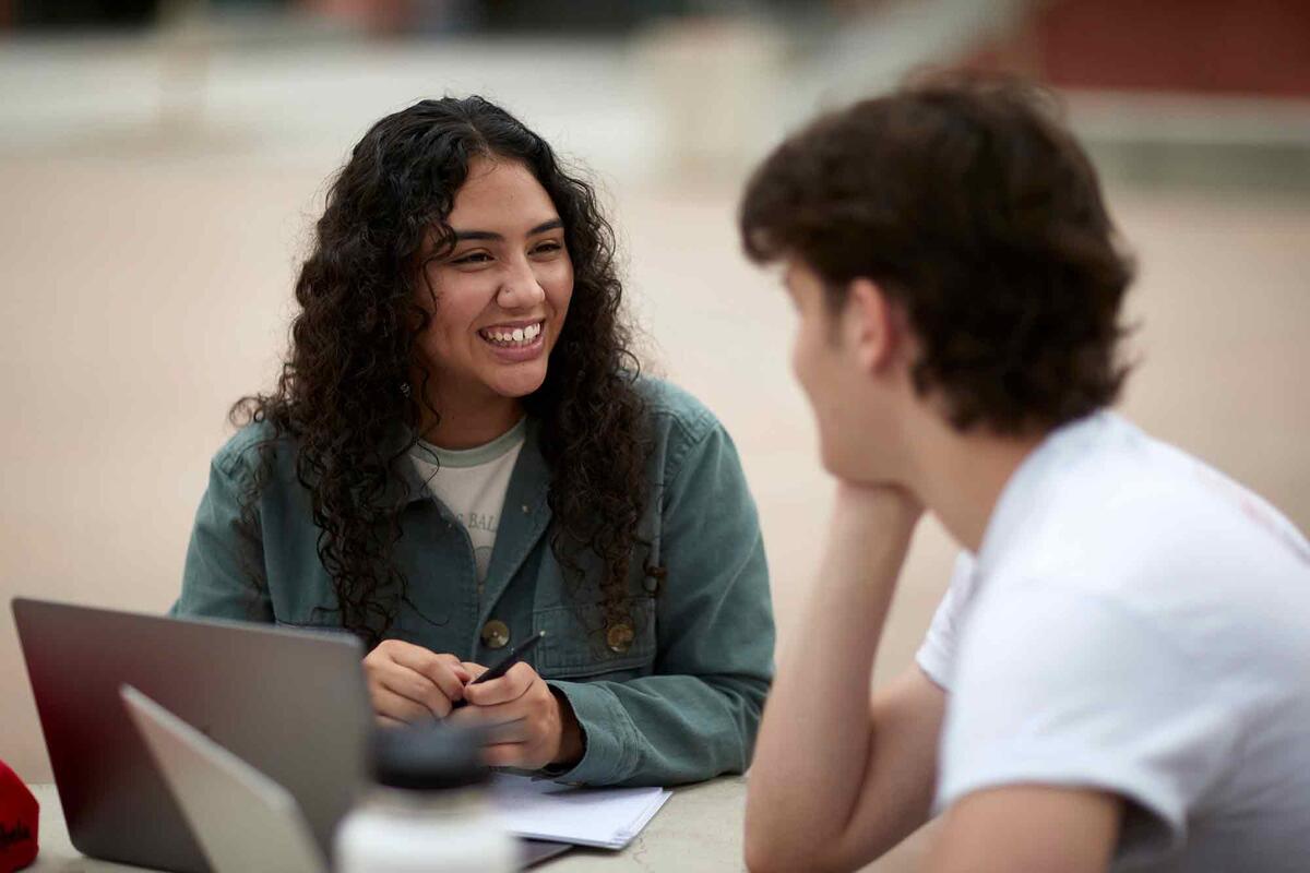 Blanca Pena (left) talks at a table with another student.