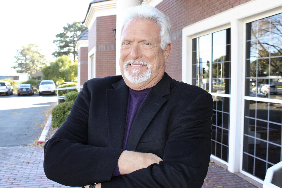Brian Lauzon stands in front of a building, arms folded in front of him.