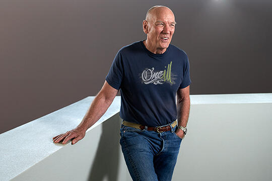 A man in a blue shirt and jeans putting their hand on a white short wall