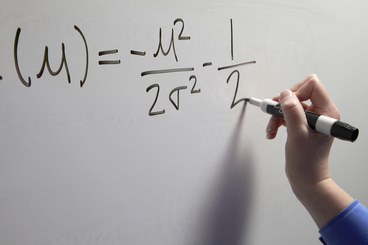 hand writing an equation on a whiteboard