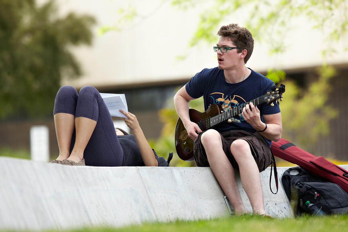 student plays guitar outside