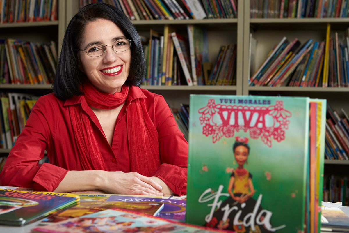 Denise Dávila sits at a table with children's books